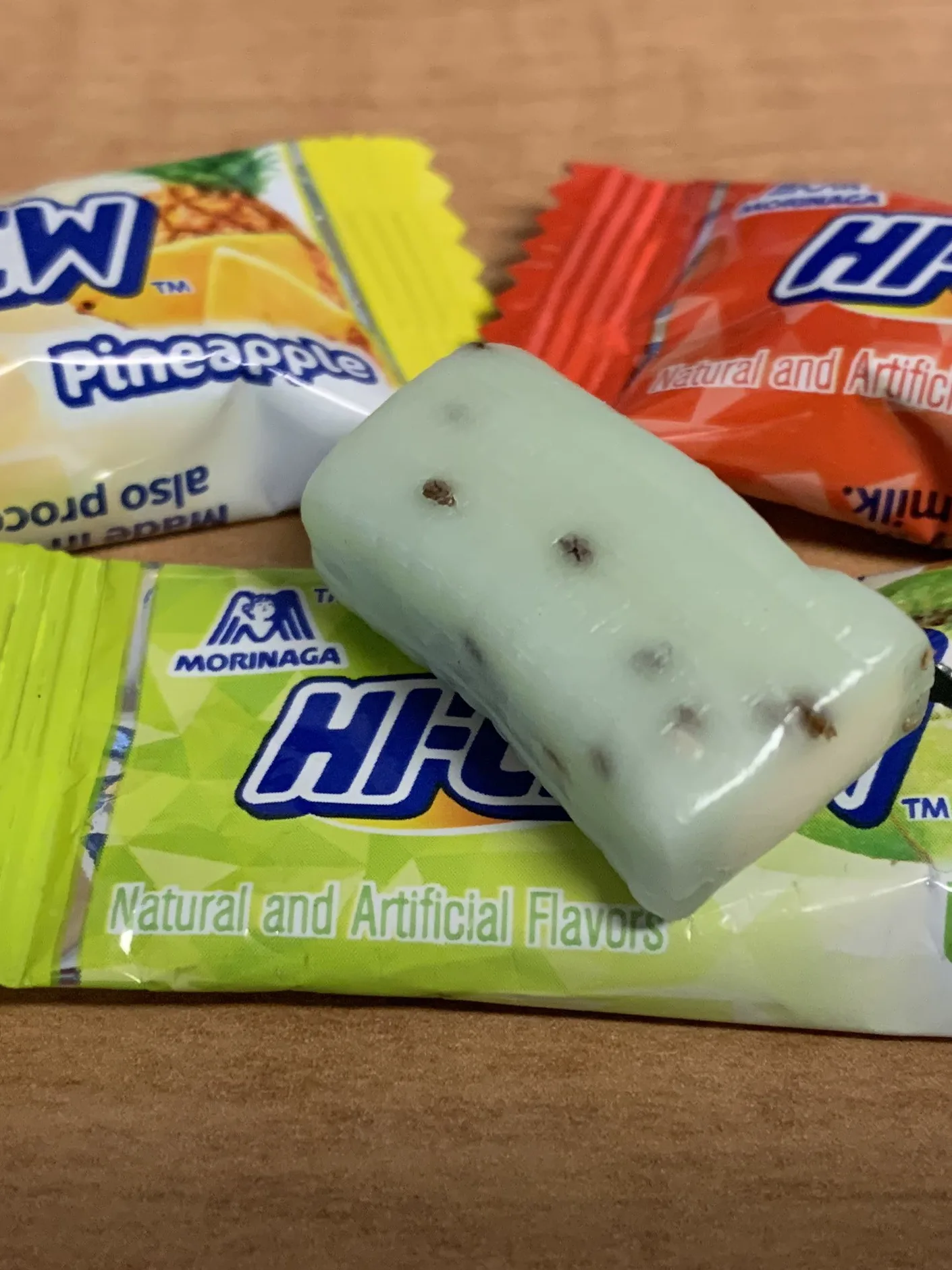 Hi-Chew: The 3 flavors of the US "tropical mix" Hi-Chew bag: "pineapple", "kiwi", and "mango". The kiwi candy is unwrapped to give a visual of the candy