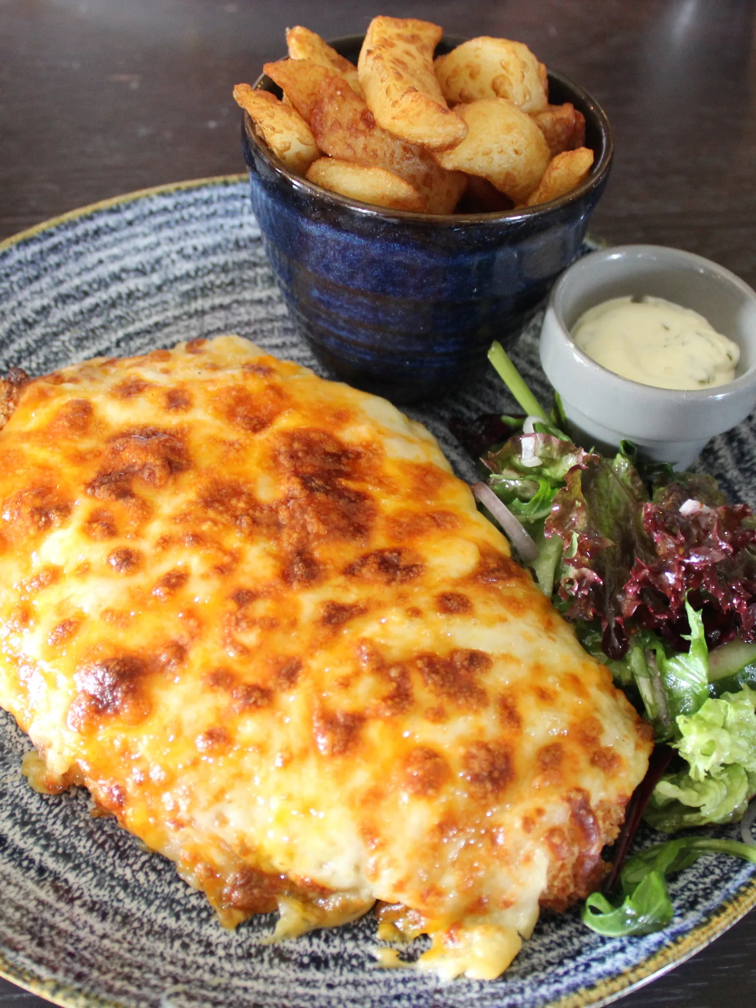 Parmo: Deep-fried chicken parmo (breaded chicken escalope topped with bechamel sauce and cheese) on a plate with chips and garlic sauce